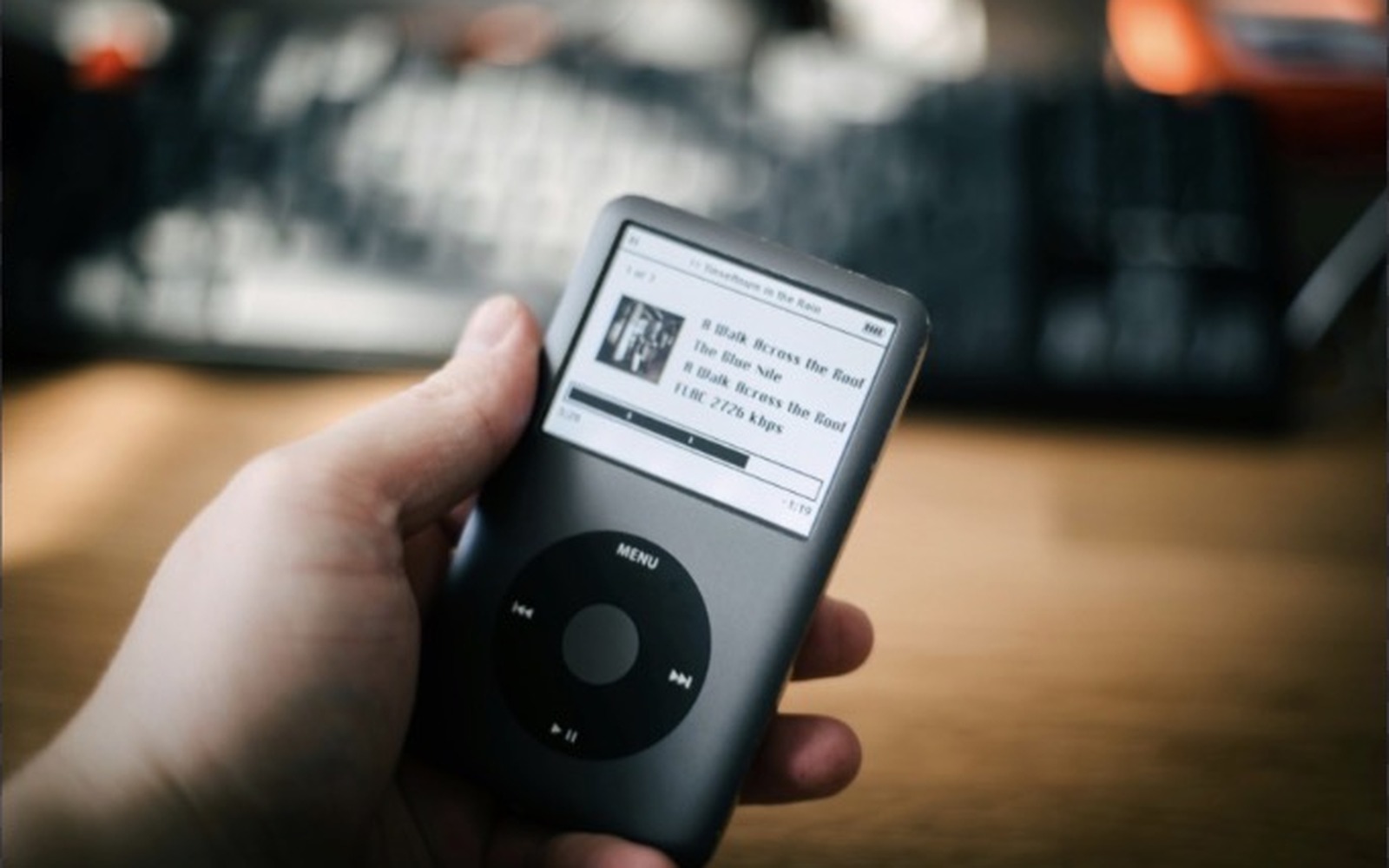 iPod Classic noir tenu en main, écran allumé sur une playlist